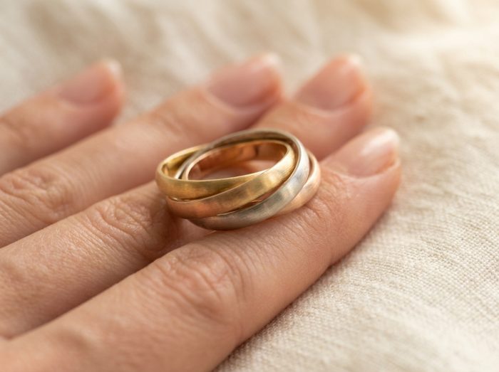 Bague trois ors en or jaune, or blanc et or rose portée sur une main de femme posée sur du lin crème